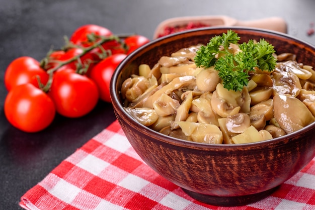 Frische köstliche würzige Dosenpilze mit Gewürzen und Kräutern in Keramikschalen auf einem dunklen Betonhintergrund