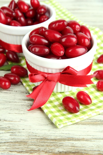 Frische Kornelbeeren in weißen Tassen auf Holztisch