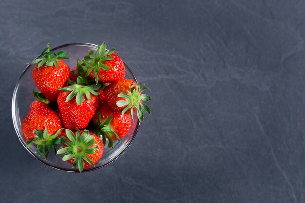 Frische leckere Erdbeeren in einer transparenten Schüssel auf einem dunkelgrauen Hintergrund