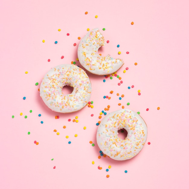 Frische leckere süße Donuts, mehrfarbige dekorative Bonbons, Zuckerwürfel auf rosa Hintergrund. Bäckereikonzept, frisches Gebäck, leckeres Frühstück, Fast Food. Flache Lage, Draufsicht.