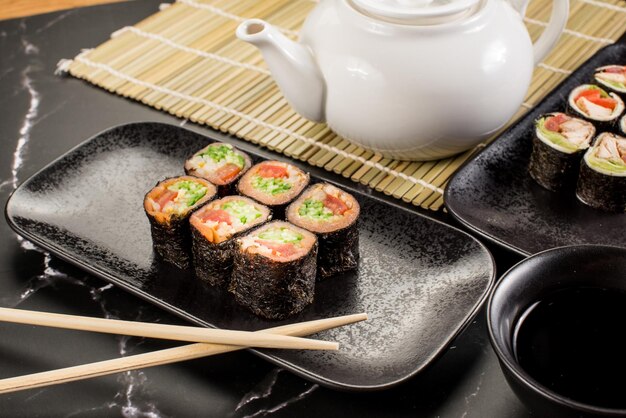 Frische leckere Sushi-Rollen mit Stöcken und Soße auf schwarzem Hintergrund
