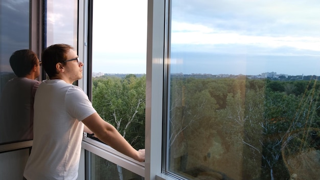 Frische Luft aus dem Fenster Seitenansicht des Menschen in der Nähe eines riesigen Fensters, das frische Luft auf den Sonnenuntergang atmet