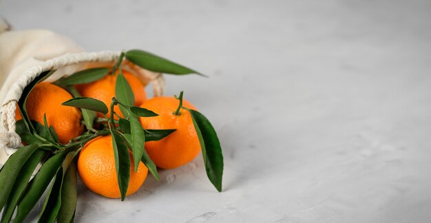 Frische mandarinen-zitrusfrüchte im flachs-sackleinenbeutel auf grauem zementhintergrund. speicherplatz kopieren.