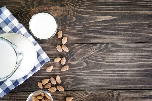 Frische Mandelmilch im Glas und im Krug auf dunklem Holztischhintergrund. Rustikaler Stil.