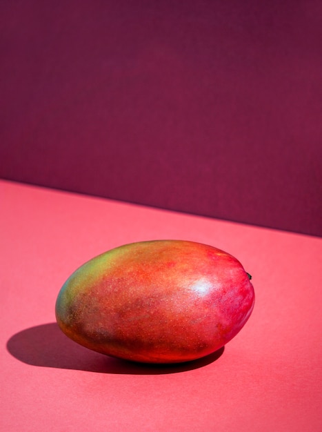 Frische Mango, Tischhintergrund im Sonnenlicht, modernes Stillleben, roter Hintergrund, grelles Licht