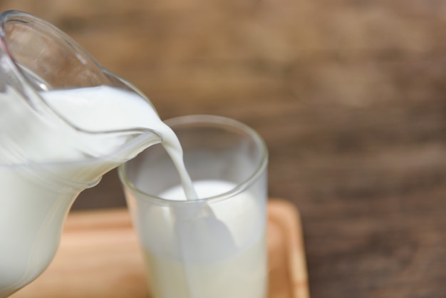 Frische Milch natürlich in einem Glaskrug und Gießen Milch in Glas auf Holzbrett