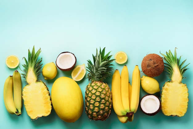 Frische organische gelbe Früchte über blauem Hintergrund. Einfarbiges Konzept mit Banane, Kokosnuss, Ananas, Zitrone, Melone.