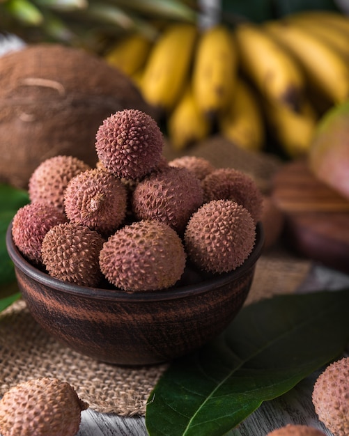 Frische organische Litschifrucht auf Bambuskorb und altem hölzernem Hintergrund, selektiver Fokus des Hintergrundes unscharf.