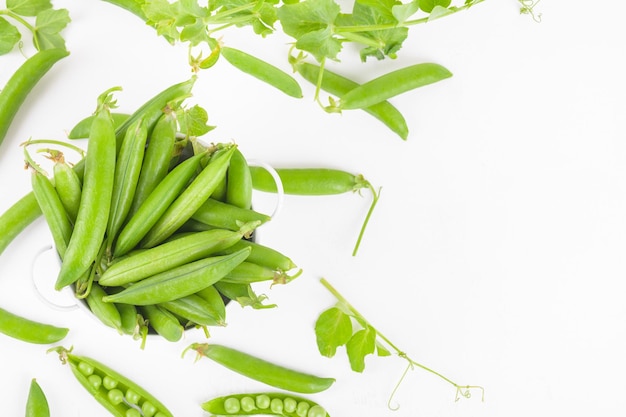 Frische organische rohe grüne Erbsenschoten in einer Schüssel mit Erbsen und Pflanzenblättern auf weißem Hintergrund Gesundes Bohnenprotein oben