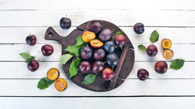 Frische Pflaumen mit Blättern Früchte auf weißem Hintergrund aus Holz Draufsicht Freier Platz für Ihren Text