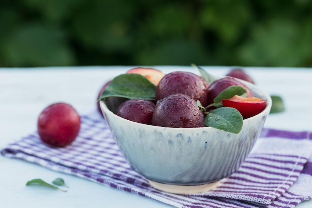 Frische Pflaumen mit Blättern in einer Schüssel auf weißem rustikalem Holztischhintergrund