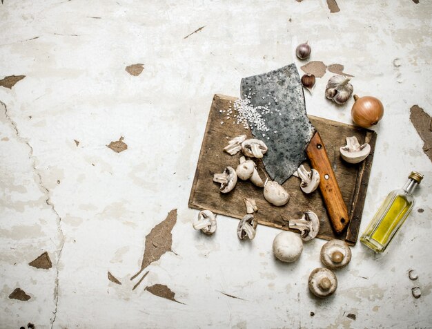 Frische Pilze gehackt mit einem Beil auf dem Brett mit Gewürzen und Olivenöl. Auf rustikalem Hintergrund.