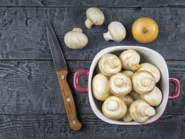 Frische Pilze in einer lila Schüssel und Messer auf einem rustikalen Holztisch