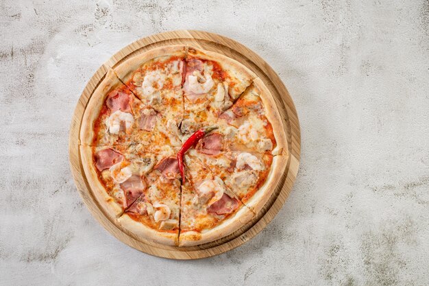 Frische Pizza mit Fleisch und Schinken auf dem konkreten Hintergrund