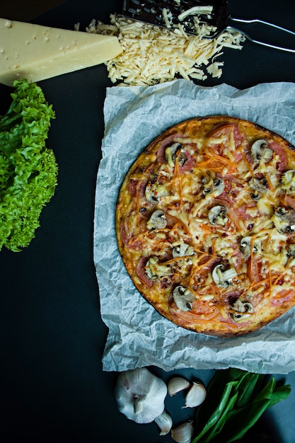 Frische Pizza mit Wurst, Tomaten, Pilzen und Käse auf einer dunklen Oberfläche