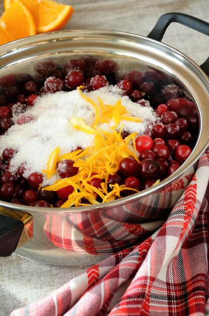 Frische Preiselbeeren mit Zucker und Orangen-Zitronenschale im Kochtopf