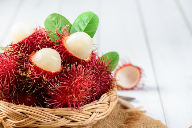 Foto frische rambutan-früchte mit blättern auf bambuskorb auf holzhintergrund