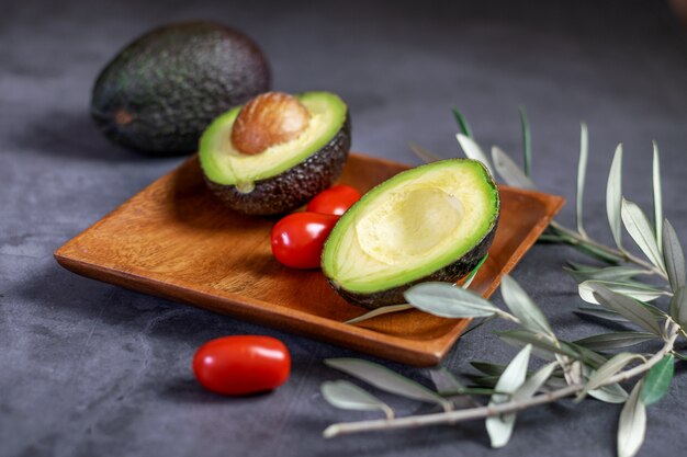 Frische reife Avocado und einige kleine Tomatenkirsche auf dem Holzteller und auf dem dunklen Hintergrund.