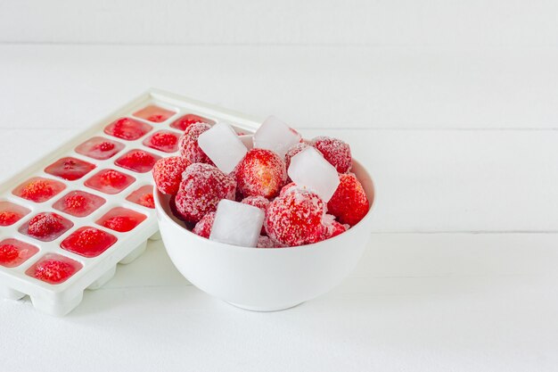 Frische reife Erdbeeren eingefroren in Eiswürfeln auf weißem Hintergrund. Gesundes Sommeressen.