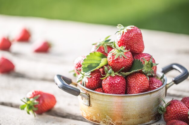 Frische reife Erdbeeren im Vintage-Küchentopf auf altem Gartentisch.