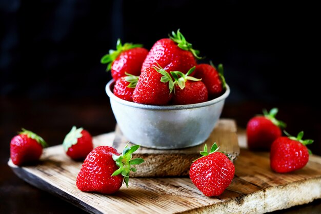 Frische reife Erdbeeren in einer Schüssel und auf einer Holzoberfläche.