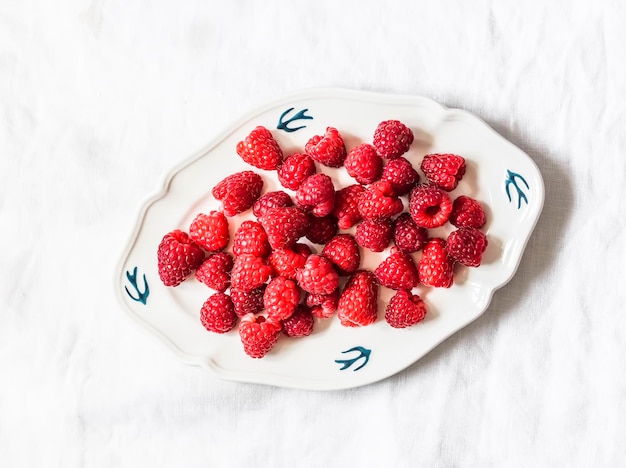 Frische reife Himbeeren auf einer Weinleseplatte auf einer Draufsicht des hellen Hintergrundes