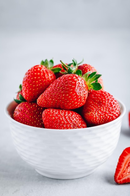 Frische reife köstliche Erdbeeren in einer weißen Schüssel auf einem grauen Steinhintergrund