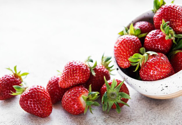 Frische reife köstliche erdbeeren in einer weißen schüssel auf einem grauen steinhintergrund