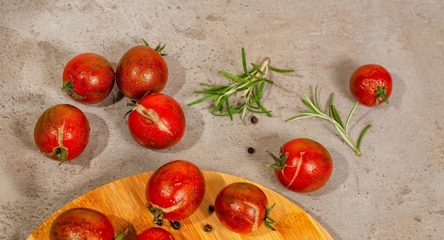 Frische reife rote Kirschtomaten aus biologischem Anbau auf der Küchentheke und dem Bambusbrett. Ansicht von oben. Zweige von Rosmarin und Pfeffer als Dekoration.