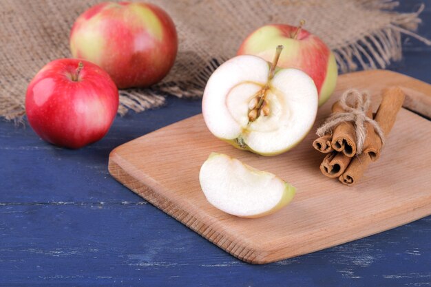 Frische reife rote Äpfel und Zimtstangen auf einem blauen Holztisch