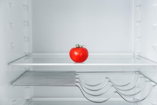 Frische reife Tomaten auf leerem Regal im Kühlschrank