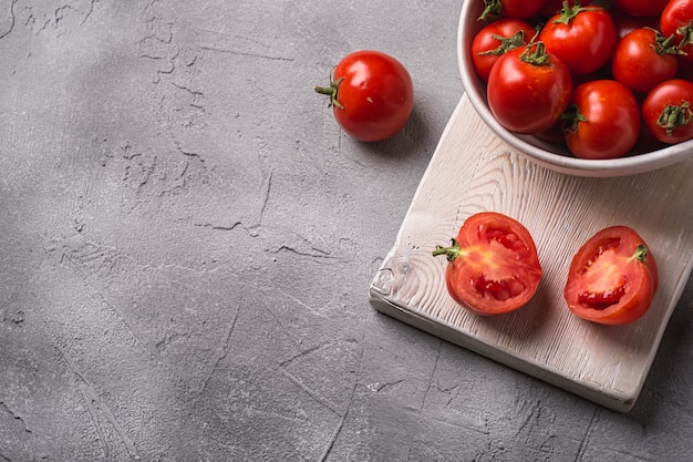 Frische reife Tomaten ganz und in Scheiben geschnitten in Schüssel und auf altem Holzschneidebrett