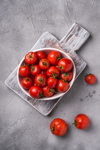 Frische reife Tomaten mit Wassertropfen in der Schüssel auf altem Holzschneidebrett