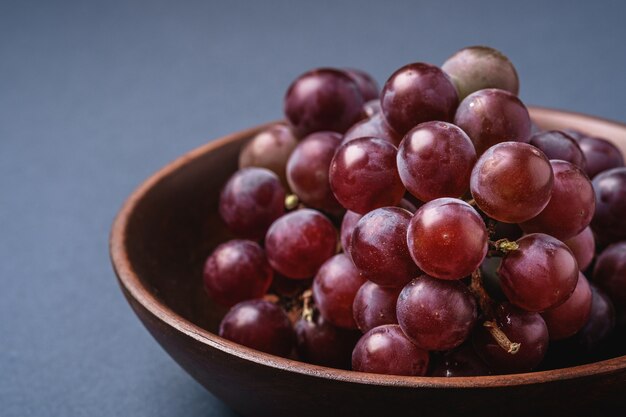 Frische reife Traubenbeeren in der braunen Holzschale auf blau grauem minimalem Hintergrund, Winkelansicht-Makro