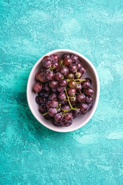 Frische reife Traubenbeeren in der Schüssel auf türkisfarbenem strukturiertem Hintergrund, Draufsicht