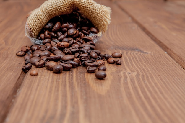 Frische Röstkaffeebohnen, die den Sack auf der Holzoberfläche herausfallen. Brown-Kaffeebohnen auf dem Tisch zerstreut von der Tasche