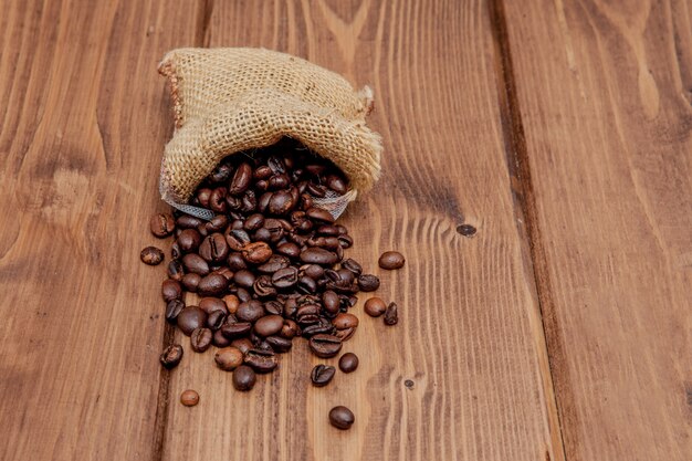 Frische Röstkaffeebohnen, die den Sack auf der Holzoberfläche herausfallen.