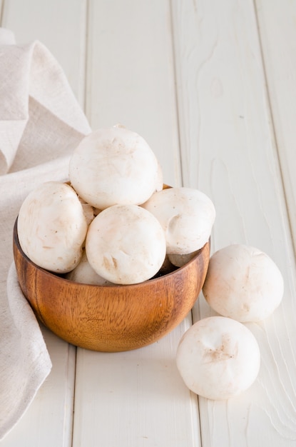 Frische rohe Champignons in einer hölzernen Schüssel auf Weiß