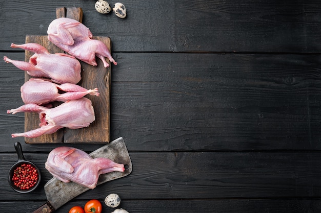 Frische rohe Fleischwachteln bereit zum Kochen, flach liegen, auf schwarzem hölzernem Hintergrund mit Platz für Text