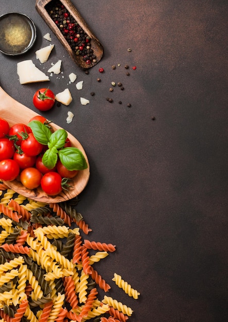 Frische rohe Fusilli-Nudeln mit Tomaten in Holzschale mit Öl und Parmesankäse mit Salz auf dunkelbraunem Hintergrund Draufsicht