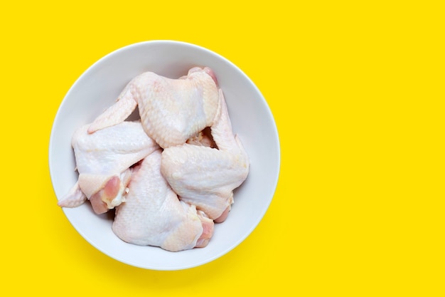 Frische rohe Hühnerflügel in weißer Schüssel auf gelbem Hintergrund.