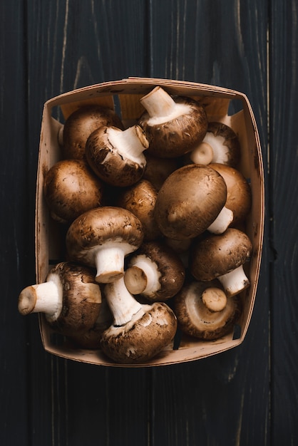 Foto frische rohe königliche champignonpilze im pappkarton auf schwarzem hölzernem schreibtisch