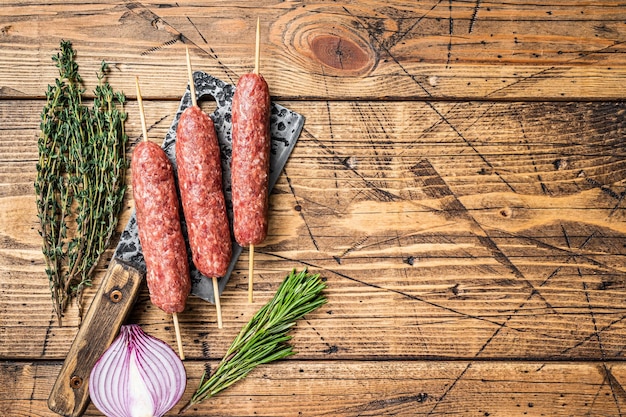 Frische rohe Kofta- oder Lula-Kebabspieße auf einem Metzgererbeil mit Kräutern. Holzhintergrund. Ansicht von oben. Platz kopieren.