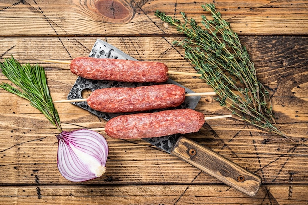 Frische rohe Kofta- oder Lula-Kebabspieße auf einem Metzgererbeil mit Kräutern. Holzhintergrund. Ansicht von oben.