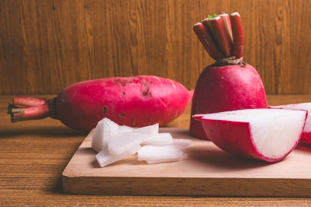 Frische rosa Rettiche auf hölzernem Schneidebrett über Holztischhintergrund.