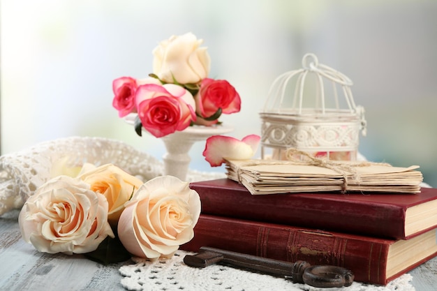 Frische Rosen mit altem Buch und Buchstaben auf farbigem Holztisch, auf hellem Hintergrund. Vintage-Konzept