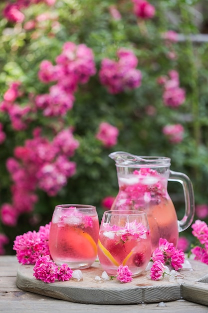 Frische Rosenlimonade mit Eis und frischen Rosen über natürlichem Garten