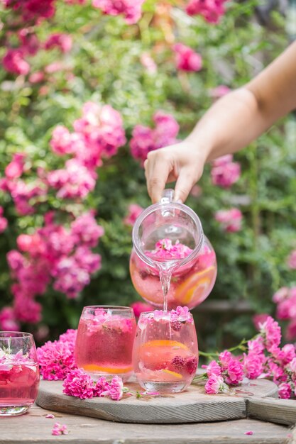 Frische Rosenlimonade mit Eis und frischen Rosen über natürlichem Garten