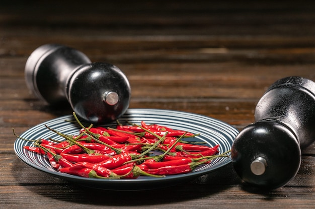 Foto frische rote chilischoten in einem teller auf einem holztisch mit einem black salt und pepper grinder set