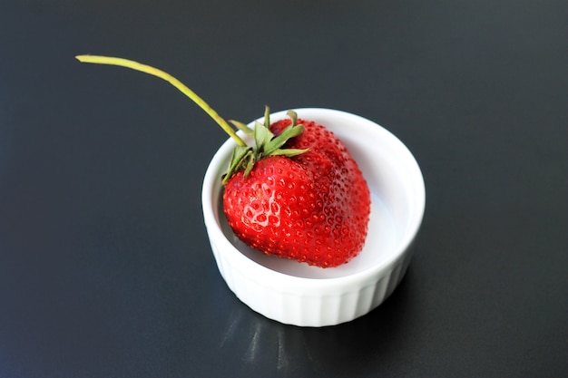 Frische rote Erdbeeren in der keramischen weißen Platte auf dunklem Hintergrund.